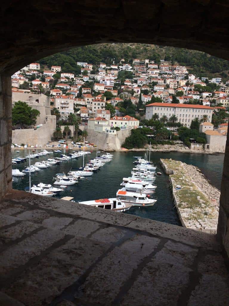 A stone window through which the beautiful Adriatic coast is visible and several yachts and boats parked.