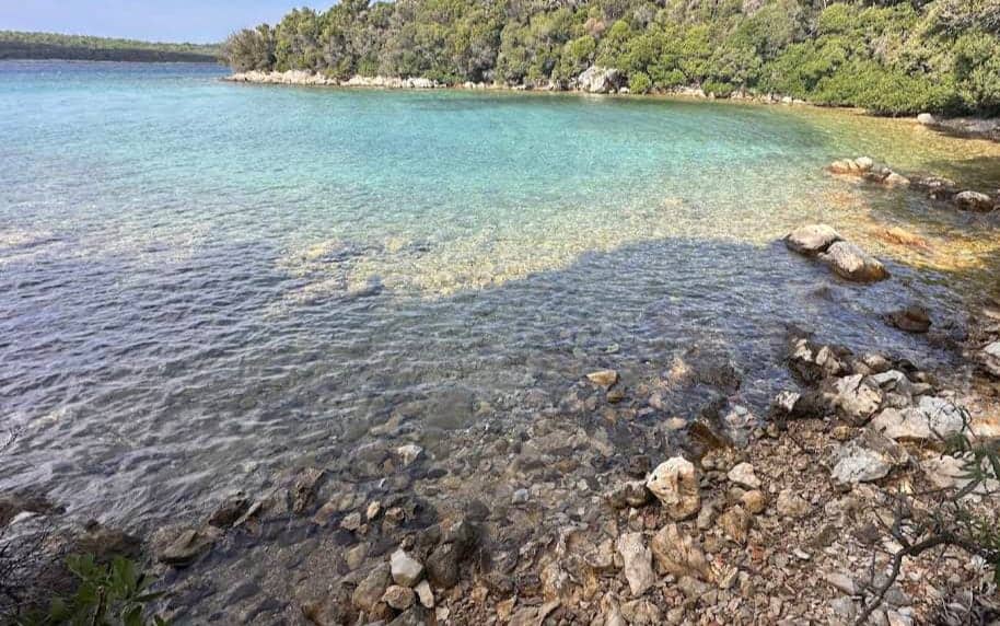 The rugged shores of Punta Križa meet calm, azure waters in a peaceful, remote setting surrounded by Mediterranean greenery, perfect for nature lovers exploring Croatia travel beaches