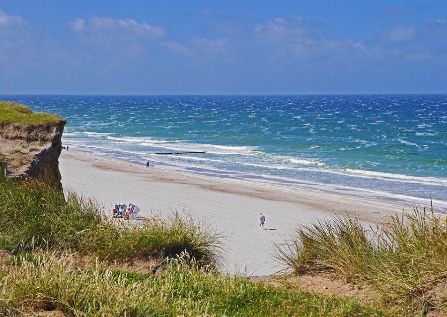 "A pristine beach on Sylt Island, Germany, with golden sand, blue waves, and grassy dunes—an idyllic spot for couples looking for coastal honeymoon destinations in Germany where they can relax and enjoy romantic seaside views