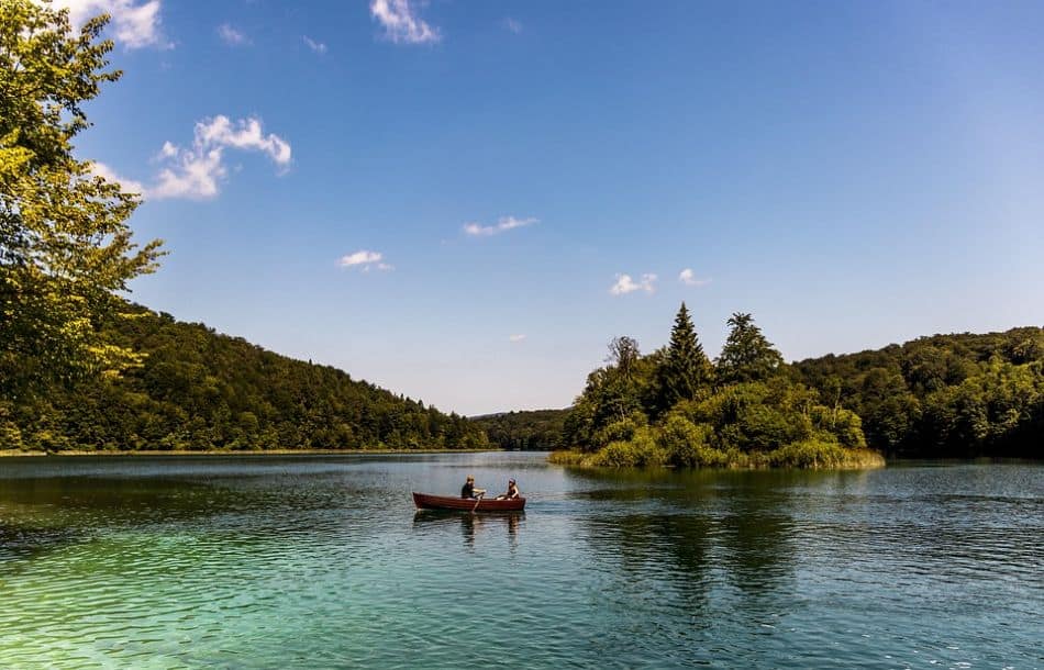 – A peaceful scene of two people rowing on the crystal-clear turquoise waters of Plitvice Lakes, surrounded by lush greenery. This UNESCO-listed park is a must-visit on a Croatia Summer Itinerary, offering breathtaking natural beauty.