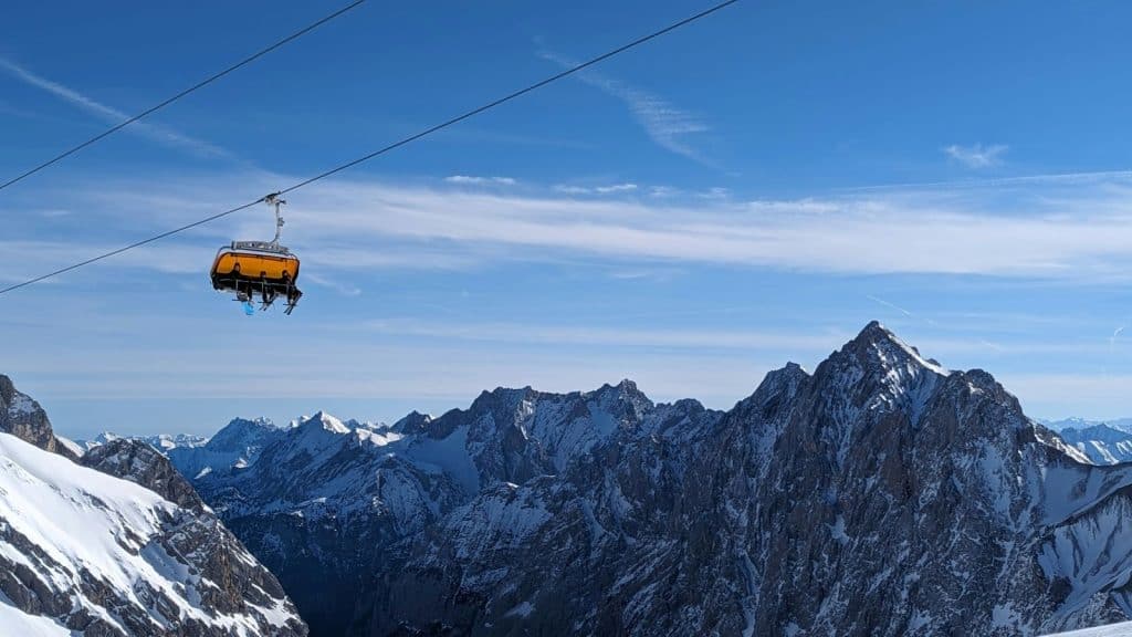 A breathtaking view of the snow-covered peaks of the Zugspitze, Germany’s highest mountain, with a bright yellow ski lift suspended over the alpine landscape. A dream destination for skiers and hikers, visiting Zugspitze is a top outdoor adventure in "Things to do in Munich."