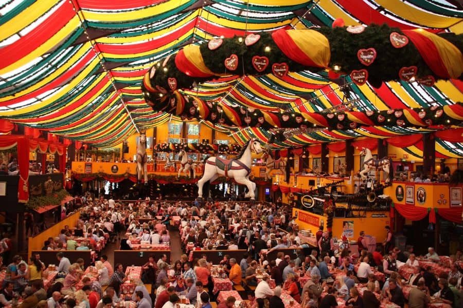  A lively Oktoberfest beer hall in Munich decorated with colorful draped banners and packed with festival-goers enjoying traditional Bavarian food and beer, an essential stop on a Munich 2 Day Itinerary.