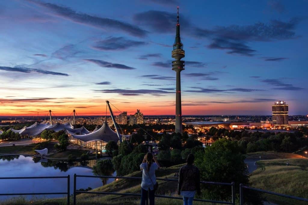 A scenic sunset view of Munich’s Olympic Park with the iconic Olympic Tower rising above modern architecture and reflective water, offering breathtaking vistas for a Munich 2 Day Itinerary.