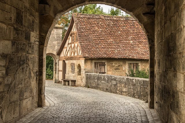 Rothenburg ob der Tauber, Bavaria, Germany – A charming cobblestone square in Rothenburg ob der Tauber in Bavaria, Germany, lined with colorful half-timbered houses. A historic well sits at the center, while vibrant pink flowers frame the foreground. This fairy-tale town is a highlight of Bavaria Germany Travel.