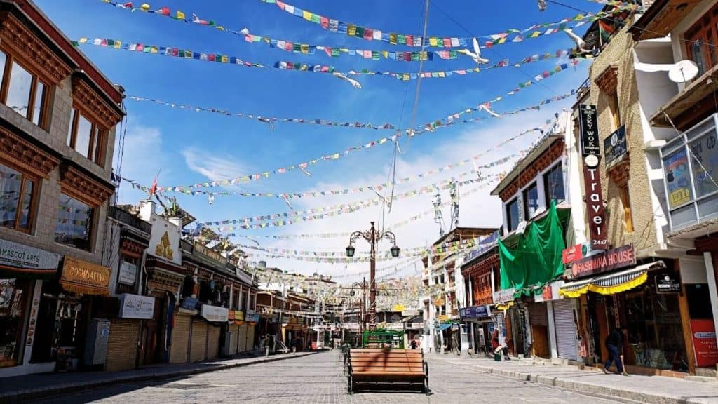 The bustling yet serene Leh Main Bazaar adorned with colorful prayer flags strung across traditional Ladakhi buildings, a vibrant shopping and sightseeing stop in a leh ladakh itinerary.