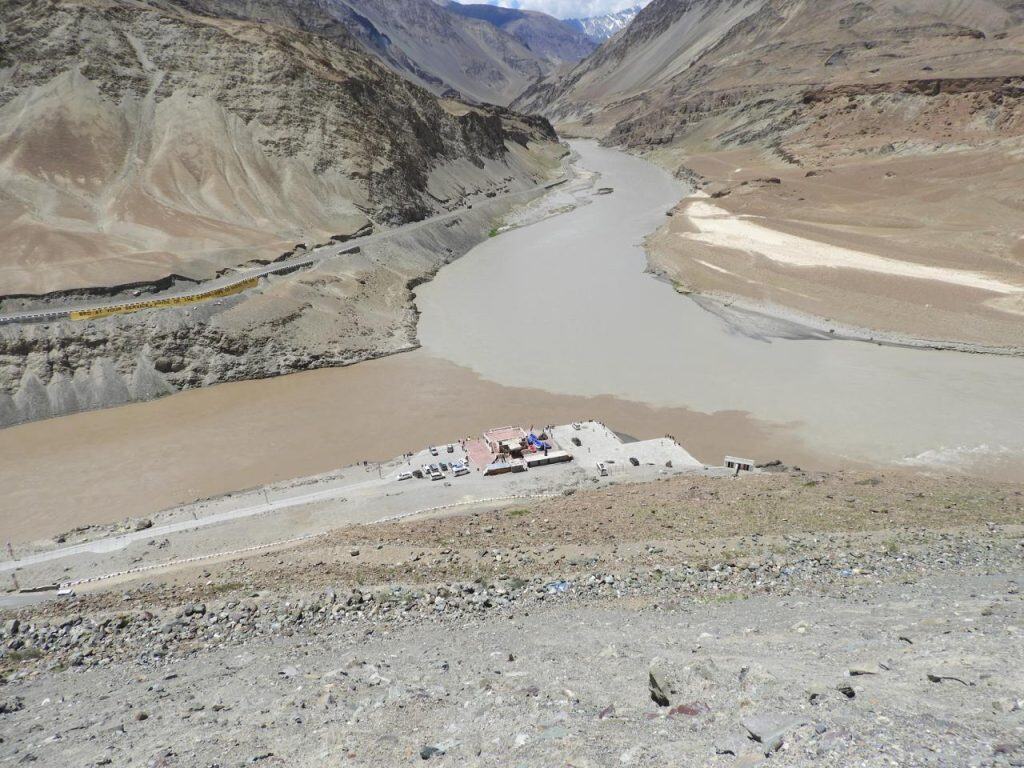 Stunning aerial view of the Zanskar River meeting the greenish Indus River at a stark mountain confluence, a visual highlight on a leh ladakh itinerary.