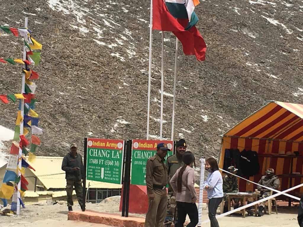 A snow-covered Chang La Pass at 17,688 feet with a signboard reading “Welcome to the Chang-La,” flanked by army huts and rugged mountains, ideal for adventurous routes in a leh ladakh itinerary.